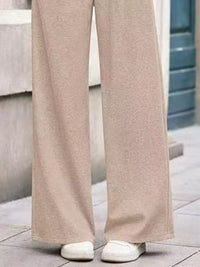 Beige wide-leg pants worn by a person on a tiled floor.