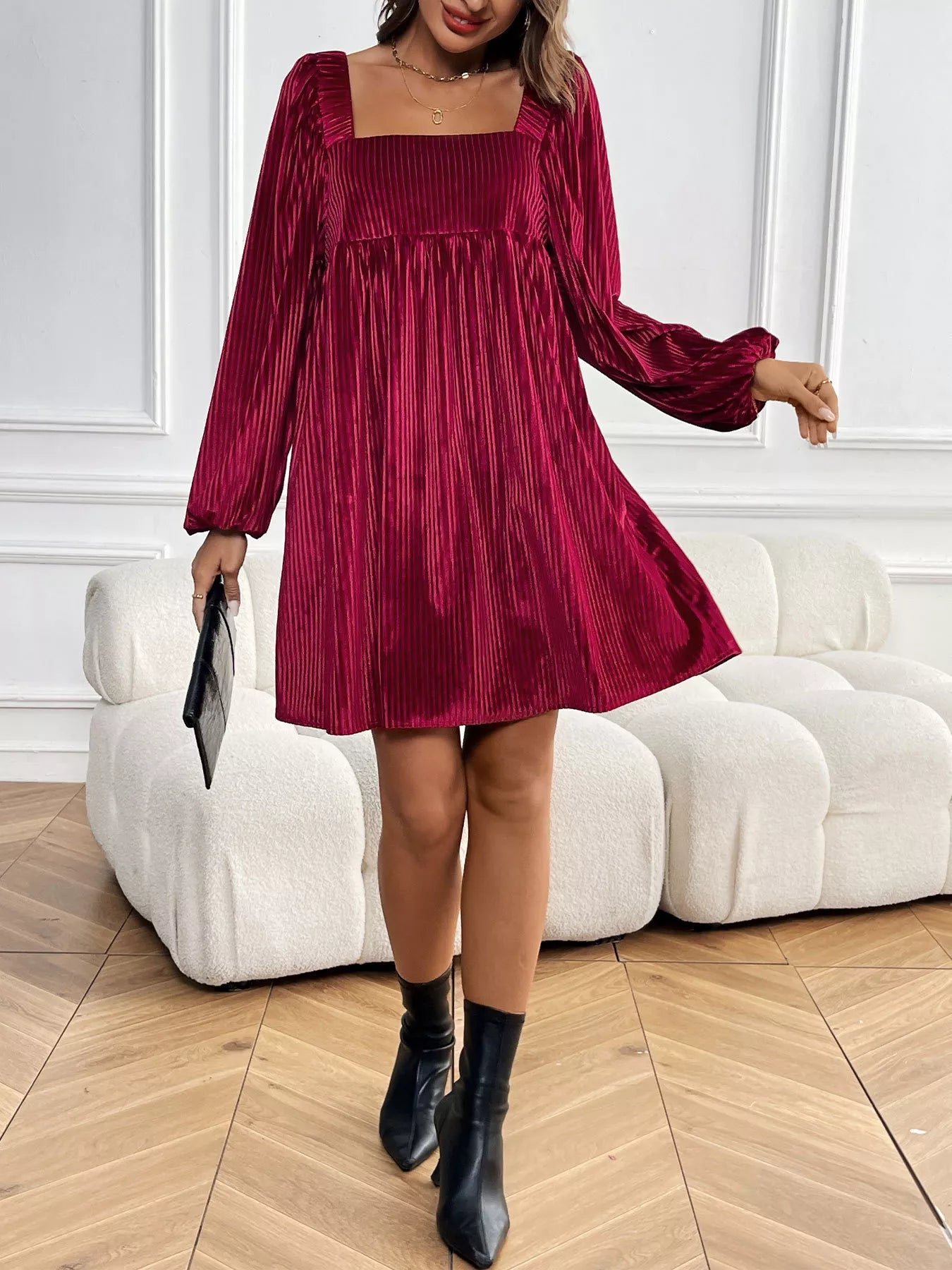 Woman wearing a burgundy pleated dress with long sleeves in an indoor setting.