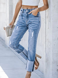 Person wearing blue jeans and a white crop top against a light gray wall.