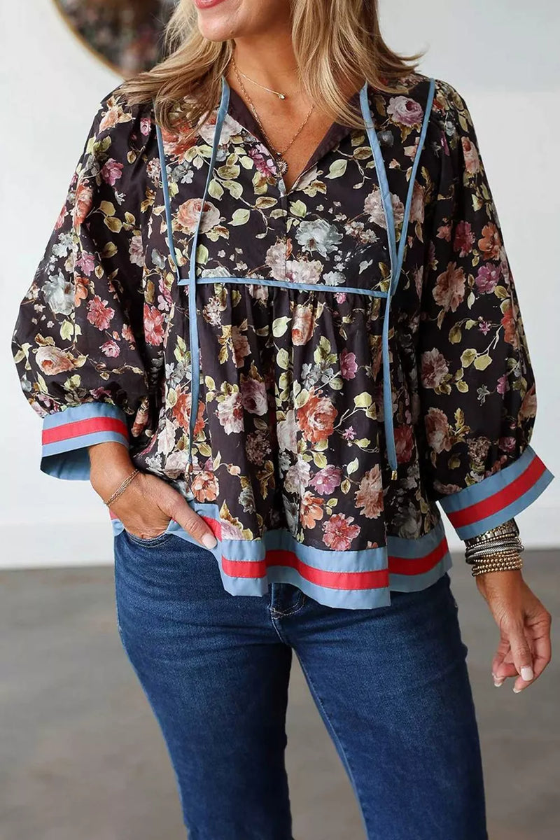 A woman wearing a dark floral long-sleeve blouse with light blue and red striped trim, paired with blue jeans.