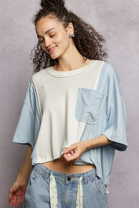 Woman wearing a light blue denim shirt over a white crop top with high-waisted jeans against a gray background
