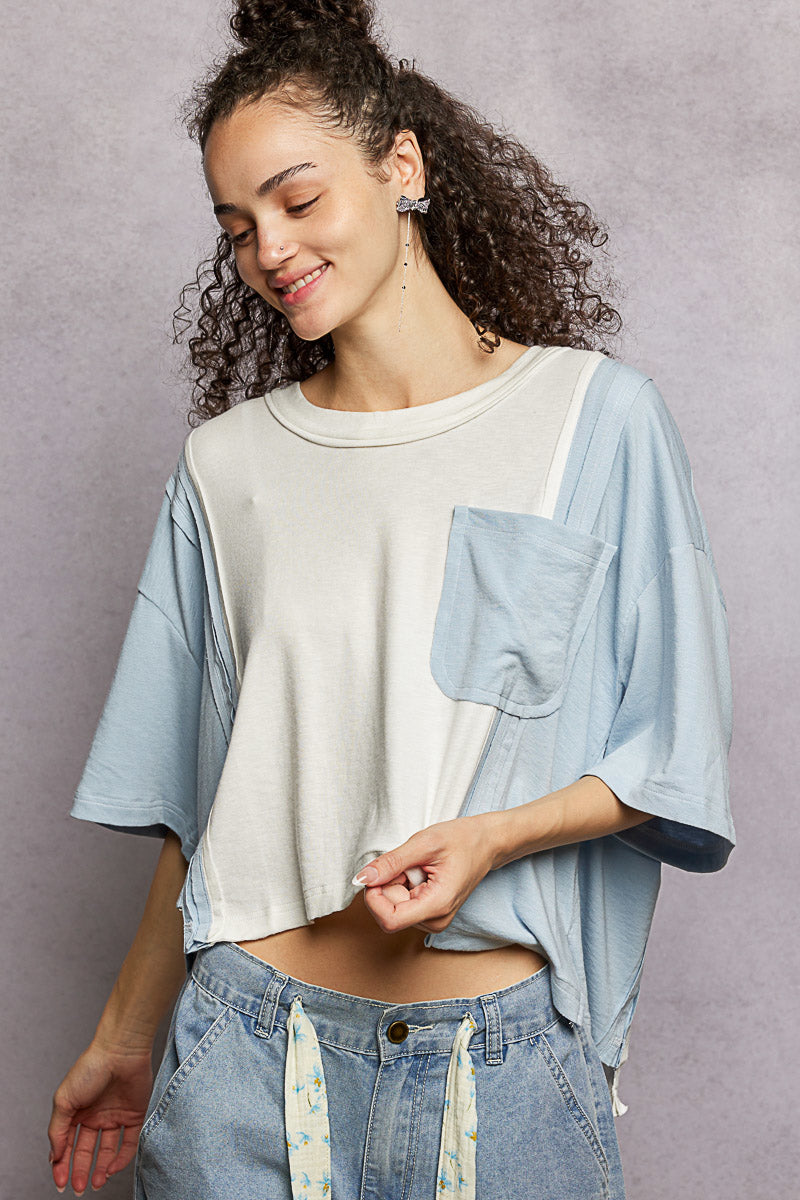 Woman wearing a light blue denim shirt over a white crop top with high-waisted jeans against a gray background