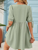 Woman wearing a light green dress with puff sleeves against a blue wall.