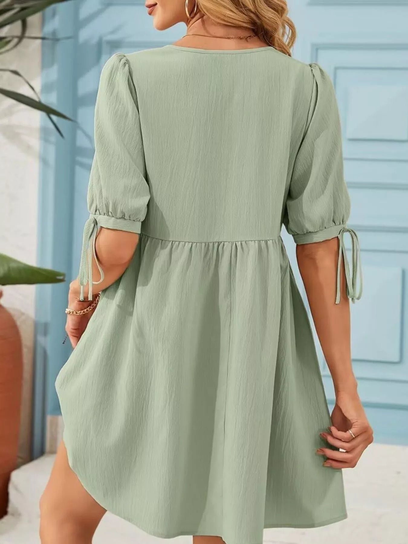 Woman wearing a light green dress with puff sleeves against a blue wall.