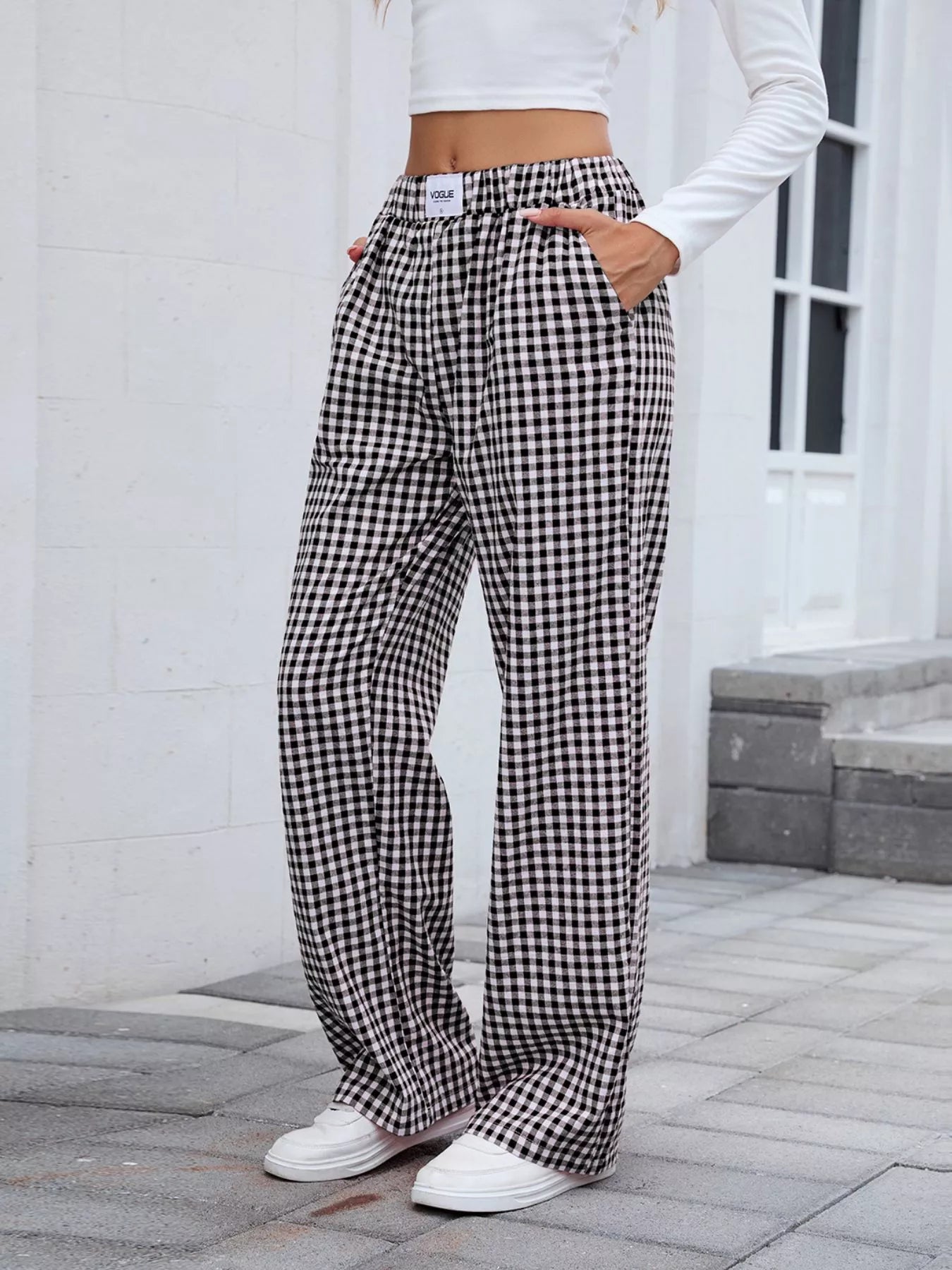 Person wearing black and white checkered pants with a white top outdoors.