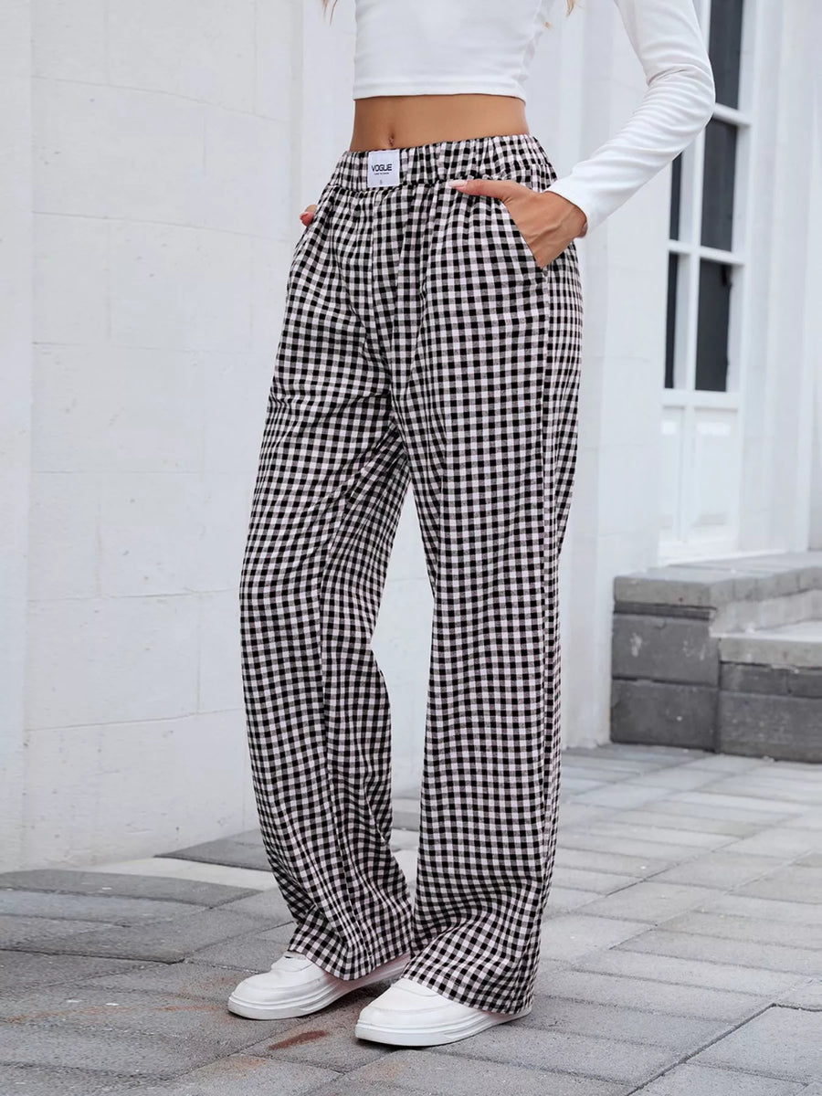 Person wearing black and white checkered pants with a white top outdoors.