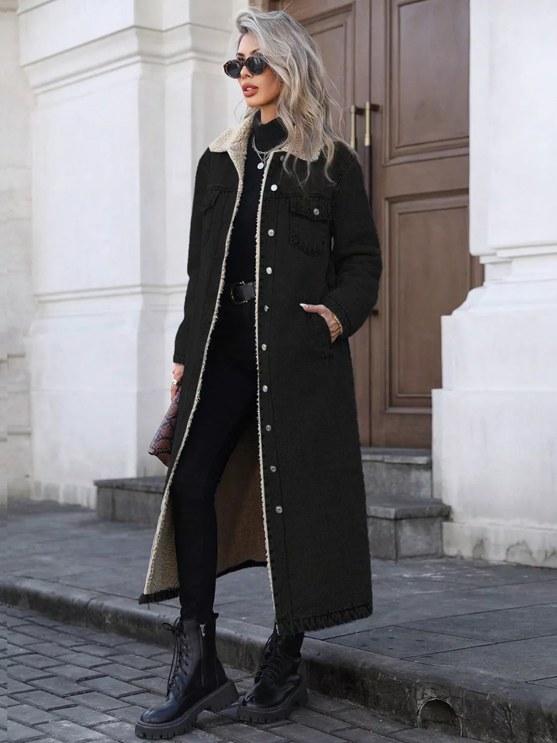 Woman wearing a long black coat with a white fur collar in an urban setting.