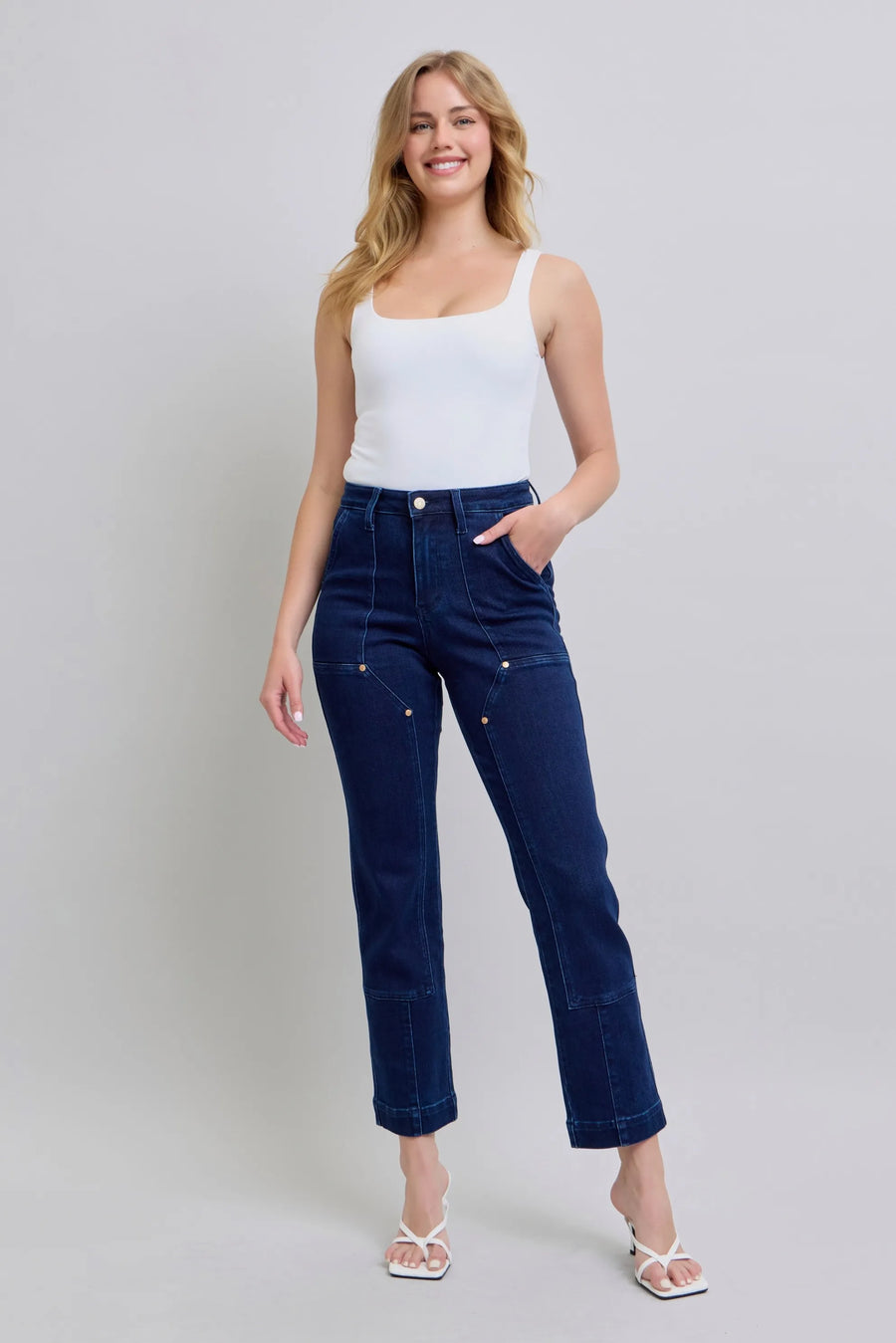 Woman wearing a white top and dark blue jeans on a plain background