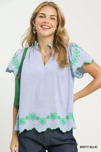 Woman wearing a light blue blouse with green floral embroidery on a white background