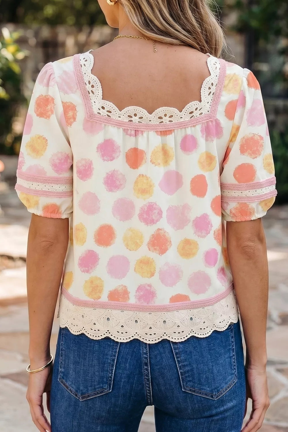Woman wearing a polka dot blouse with lace details and blue jeans outdoors.