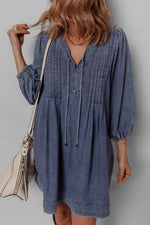 Woman wearing a blue denim dress with a beige handbag against a plain background