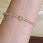 Pink beaded bracelet with a gold clasp on a wrist against a neutral background