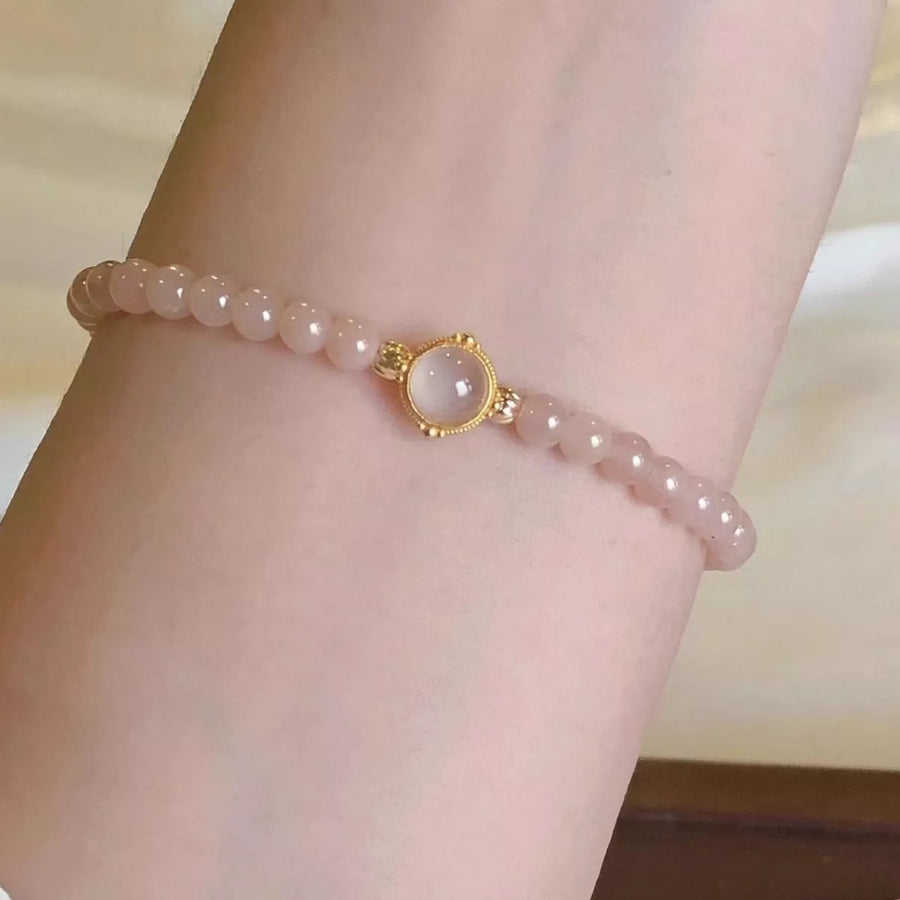 Pink beaded bracelet with a gold clasp on a wrist against a neutral background