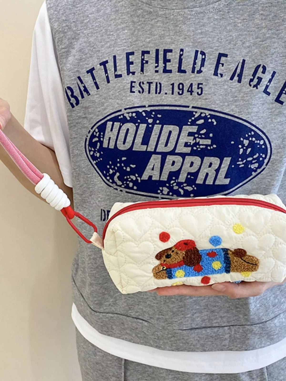 Person holding a white pouch with a dog design, wearing a gray 'Battlefield Eagle' shirt.