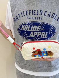 Person holding a white pouch with a dog design, wearing a gray 'Battlefield Eagle' shirt.