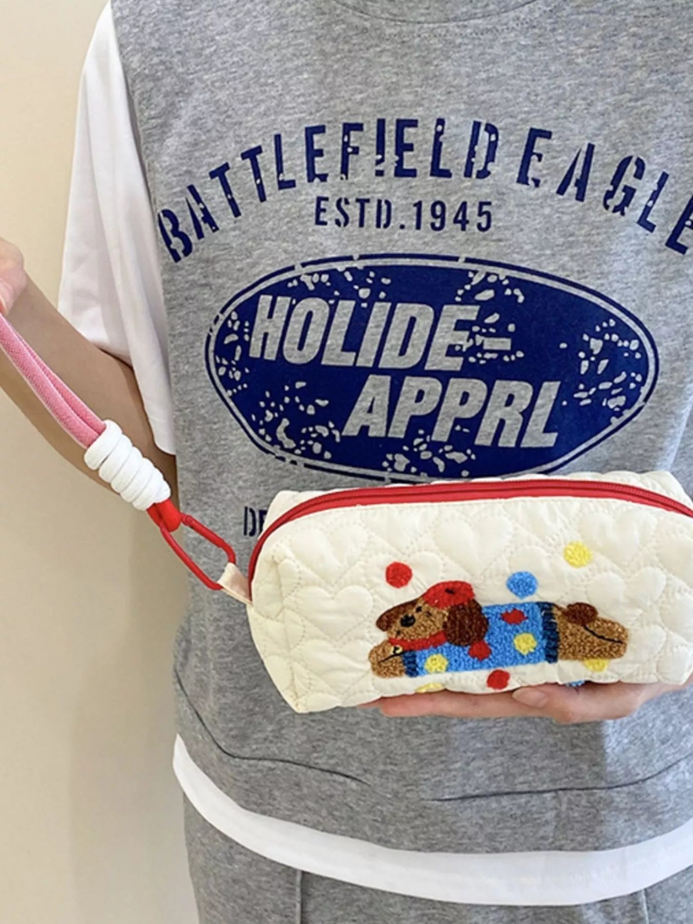 Person holding a white pouch with a dog design, wearing a gray 'Battlefield Eagle' shirt.
