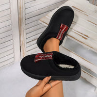 Black slippers with red and white pattern held by a hand against a light background