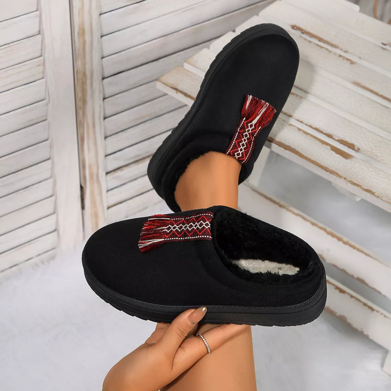 Black slippers with red and white pattern held by a hand against a light background