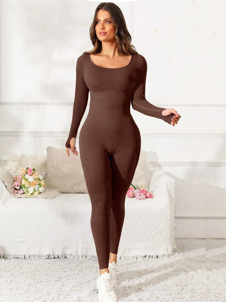 Woman wearing a brown bodysuit in a white room with a couch and flowers.