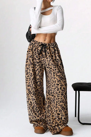 Person wearing leopard print pants and a white top on a plain background