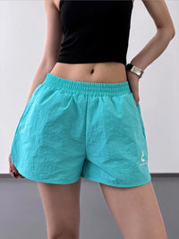 Person wearing turquoise shorts and a black top on a plain background
