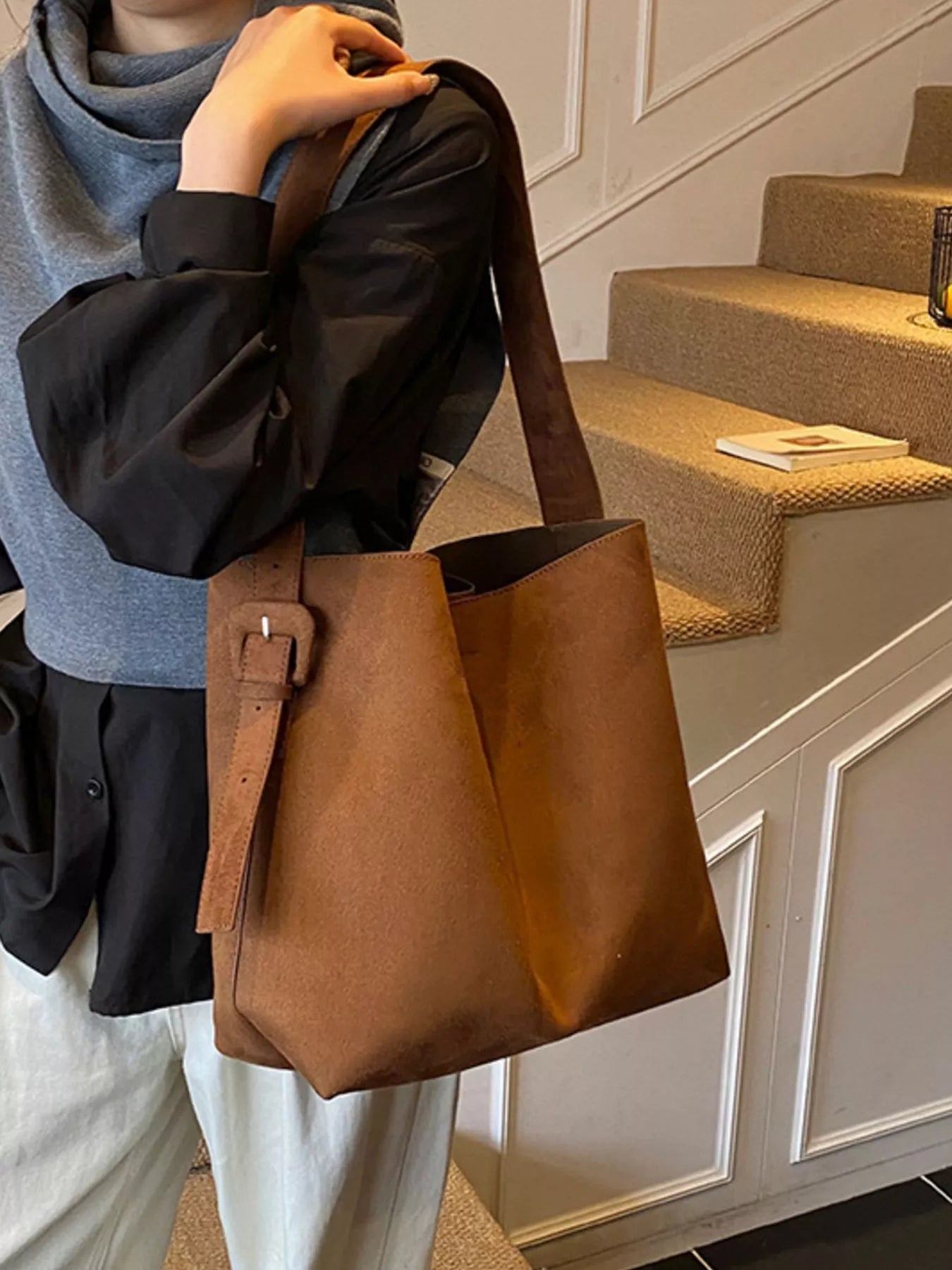 Person holding a brown leather bag indoors with steps in the background