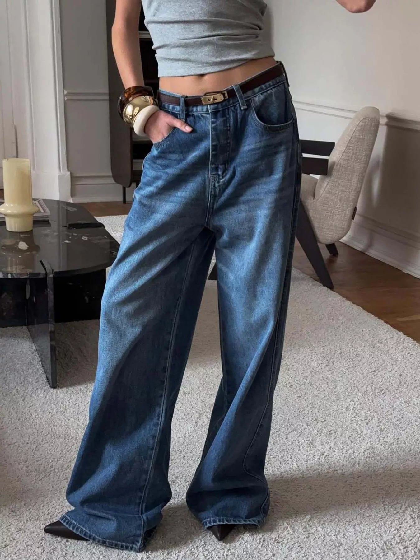 Person wearing blue wide-leg jeans in a room with a table and chair.