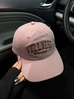 Pink cap with 'Wellness' text held inside a car.