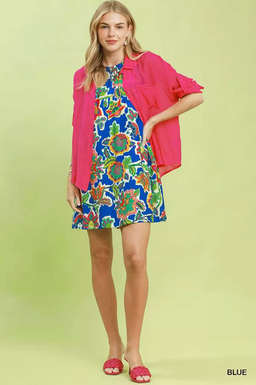 Woman wearing a colorful floral dress with a pink jacket on a light green background