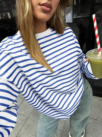 Person wearing a blue and white striped sweater holding a green drink with a straw.