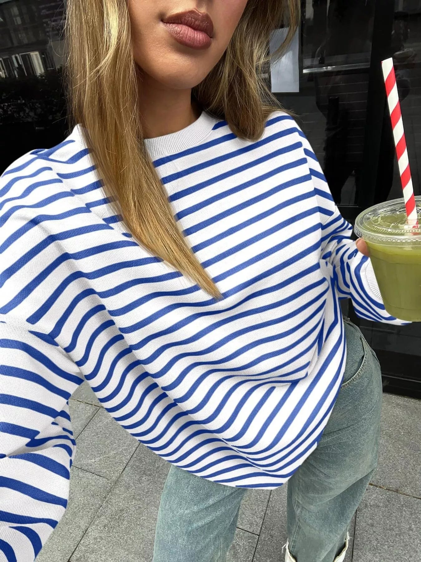 Person wearing a blue and white striped sweater holding a green drink with a straw.