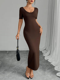 Woman wearing a brown dress holding a black handbag against a gray background