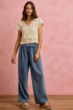 Woman wearing a lace top and wide-leg jeans against a pink background