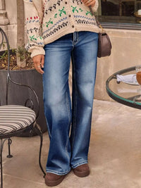 Person wearing a patterned sweater and blue jeans standing outdoors.