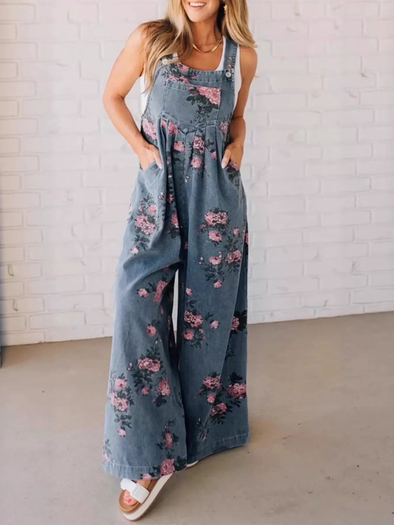Woman wearing a floral denim jumpsuit against a white brick wall.