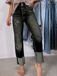 Person wearing black and gray distressed jeans with a background of hanging jeans.
