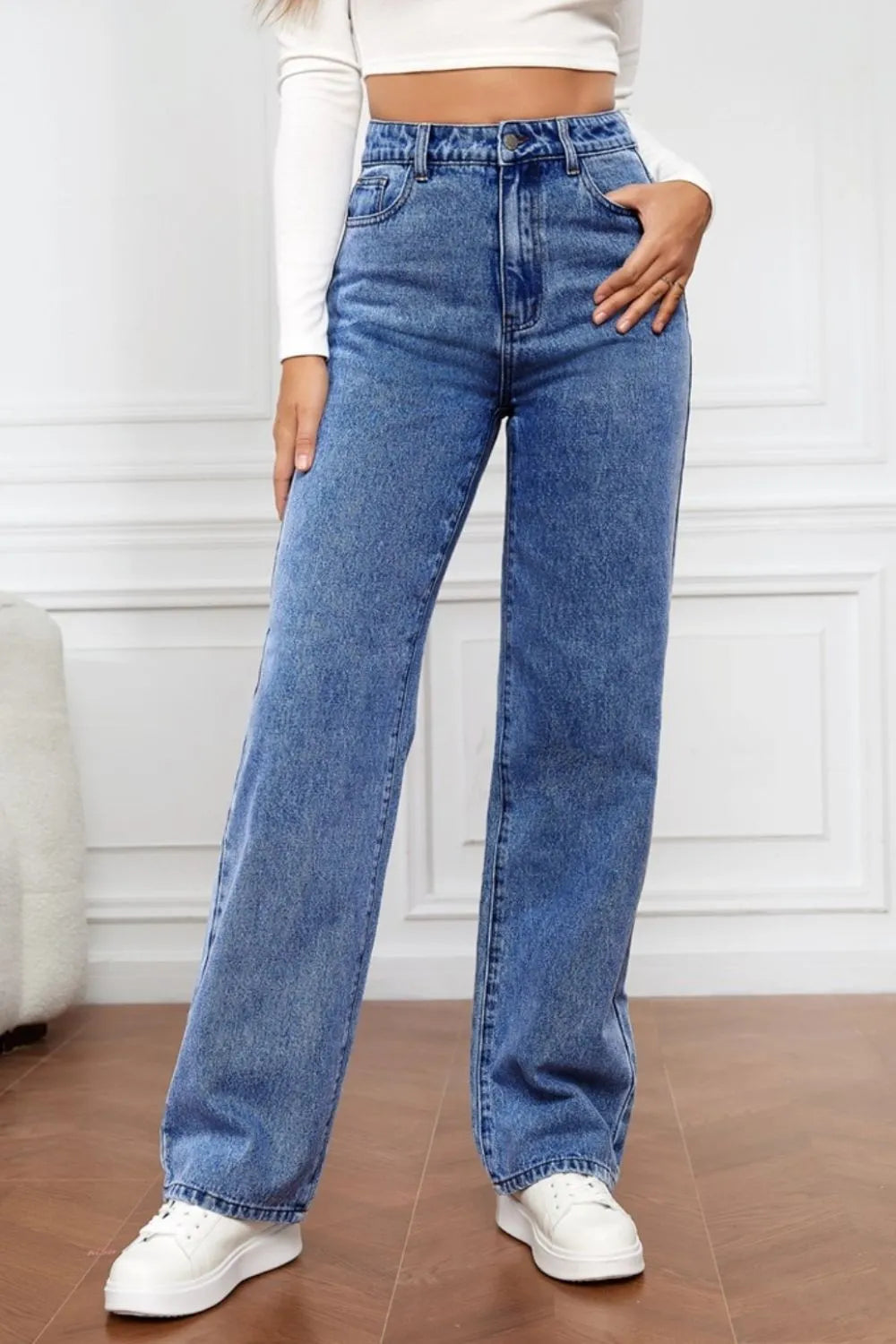 Person wearing blue jeans and white sneakers in a minimalistic setting