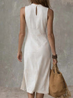 Woman wearing a white dress holding a brown woven bag against a gray background