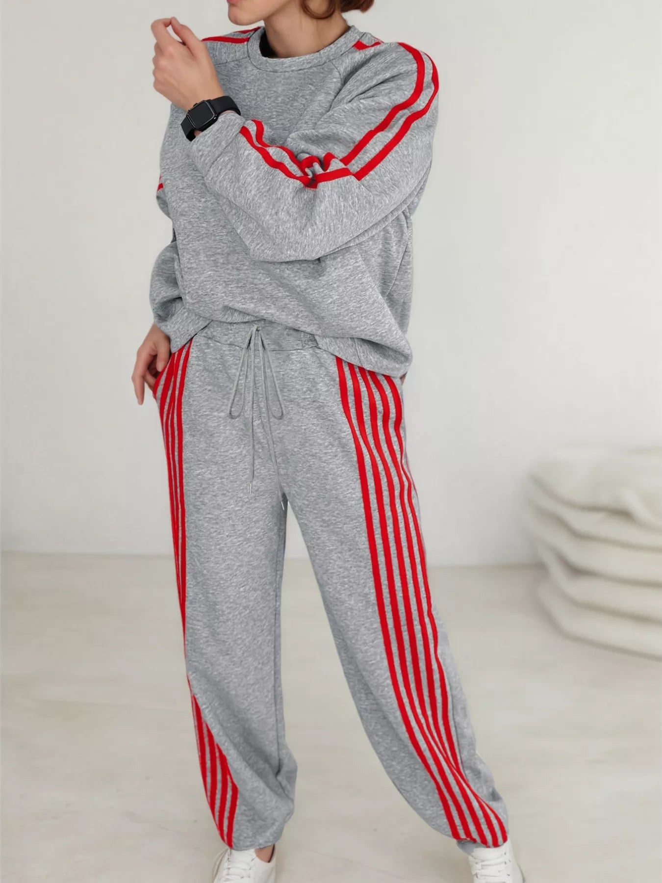 Person wearing a gray tracksuit with red stripes on a white background