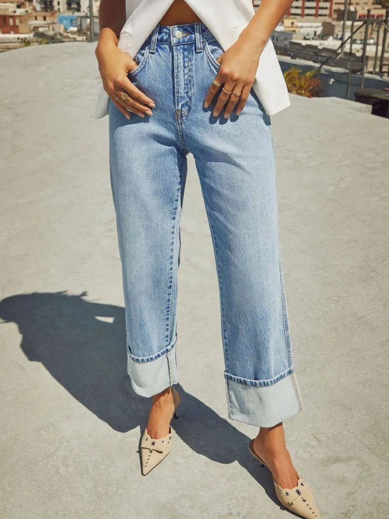 Person wearing light blue jeans on a rooftop with a blurred cityscape background