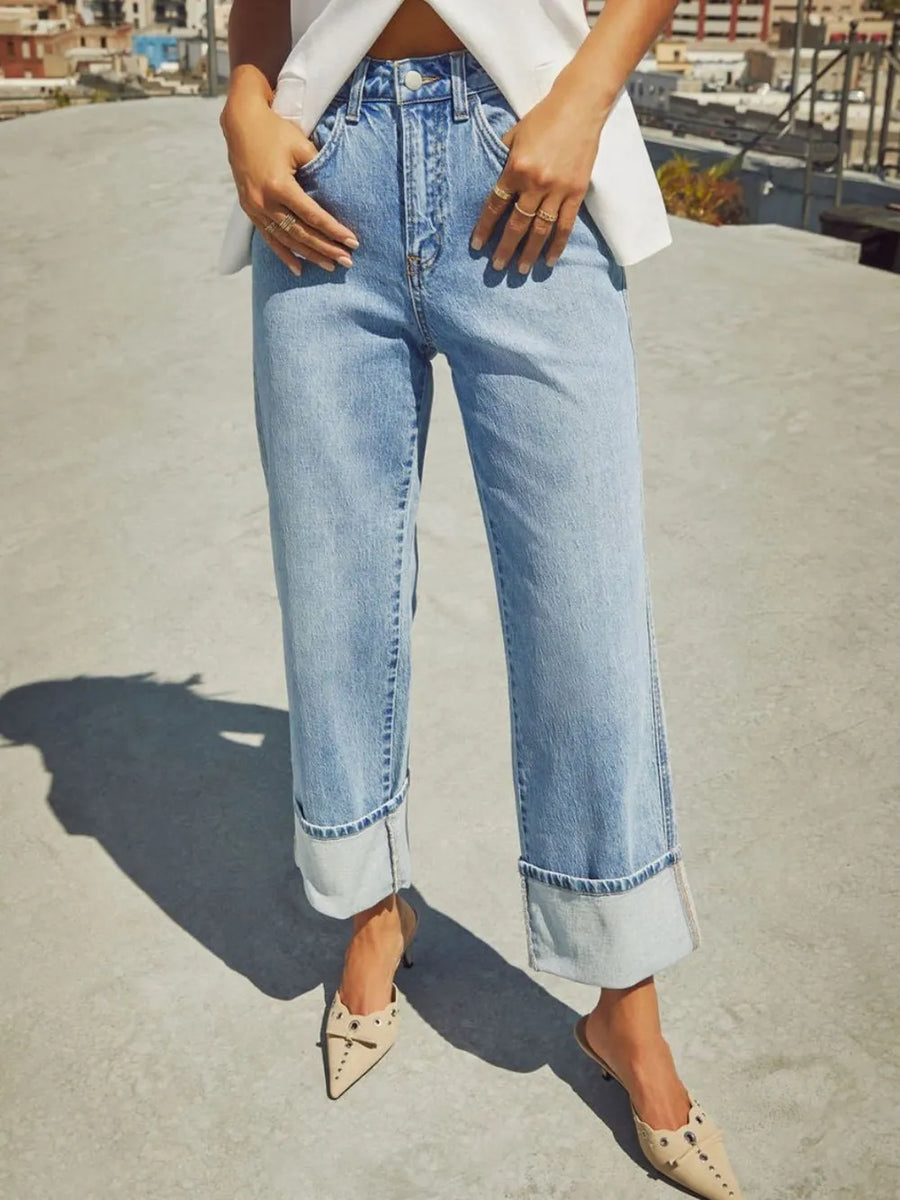 Person wearing light blue jeans on a rooftop with a blurred cityscape background