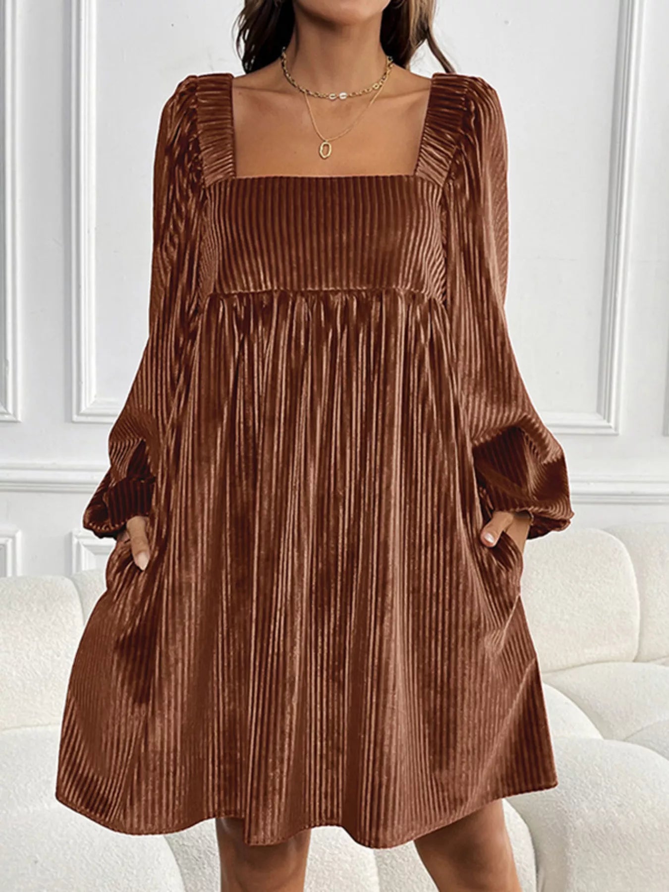 Brown pleated dress worn by a person in a minimalistic setting