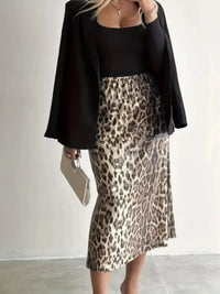 Person wearing a black top and leopard print skirt with a plain background