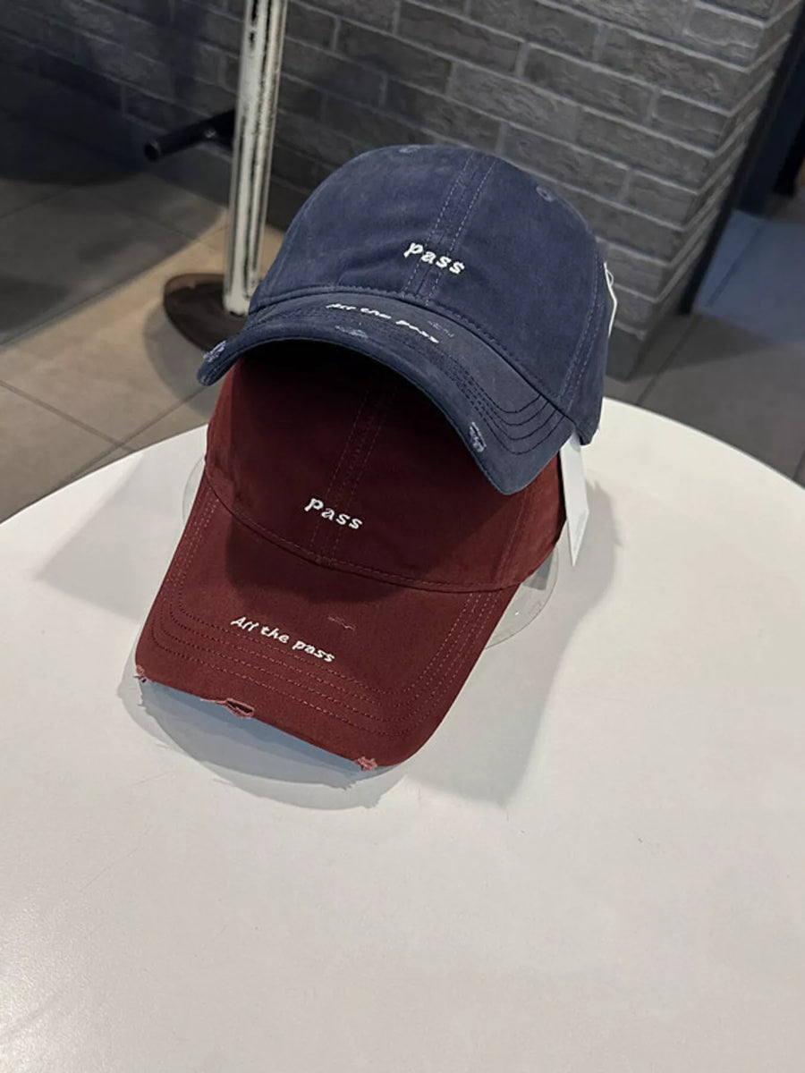 Two baseball caps, one blue and one red, with 'PASS' branding on a white surface.