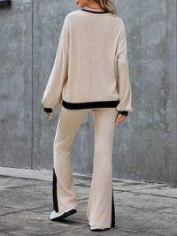 Person wearing a beige ribbed sweater and pants with black trim against a gray wall.