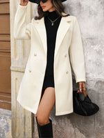 Woman wearing a white coat over a black dress, standing against a textured wall.