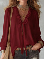 Red blouse with ruffled details and gold accessories on a neutral background