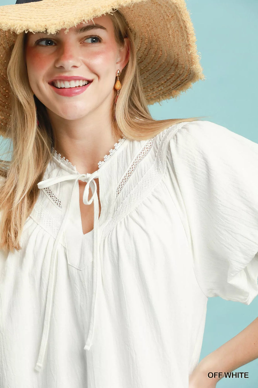 Woman wearing a white blouse and straw hat against a light blue background
