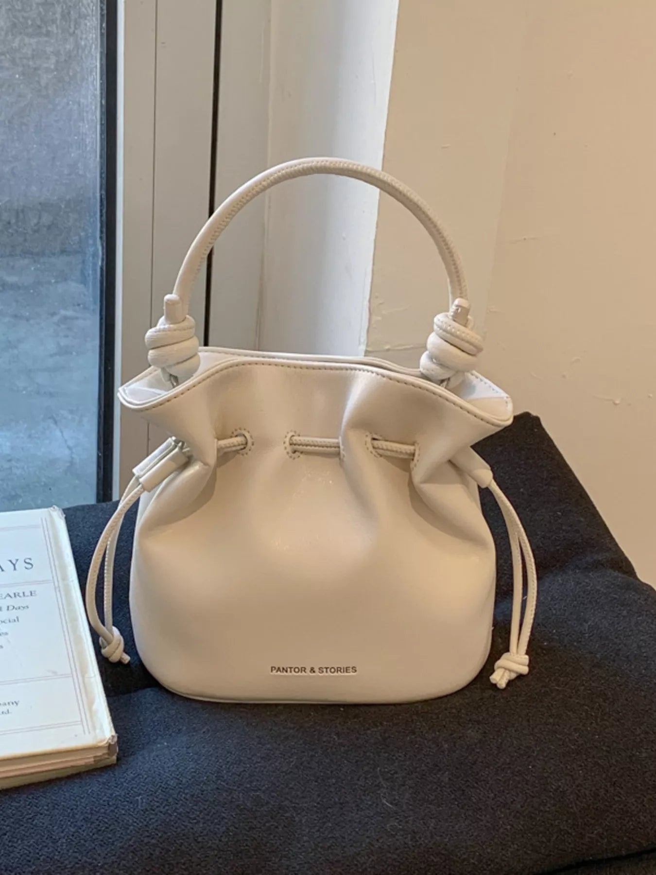 Beige handbag with drawstring on a dark surface near a window