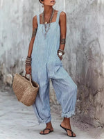 Woman wearing a blue striped jumpsuit holding a woven bag against a textured wall.